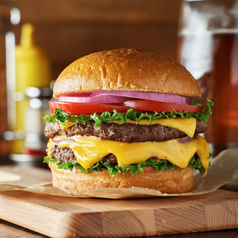 A double cheeseburger with lettuce, tomato, and red onion on a wooden board at Motown Bowls & Grill.