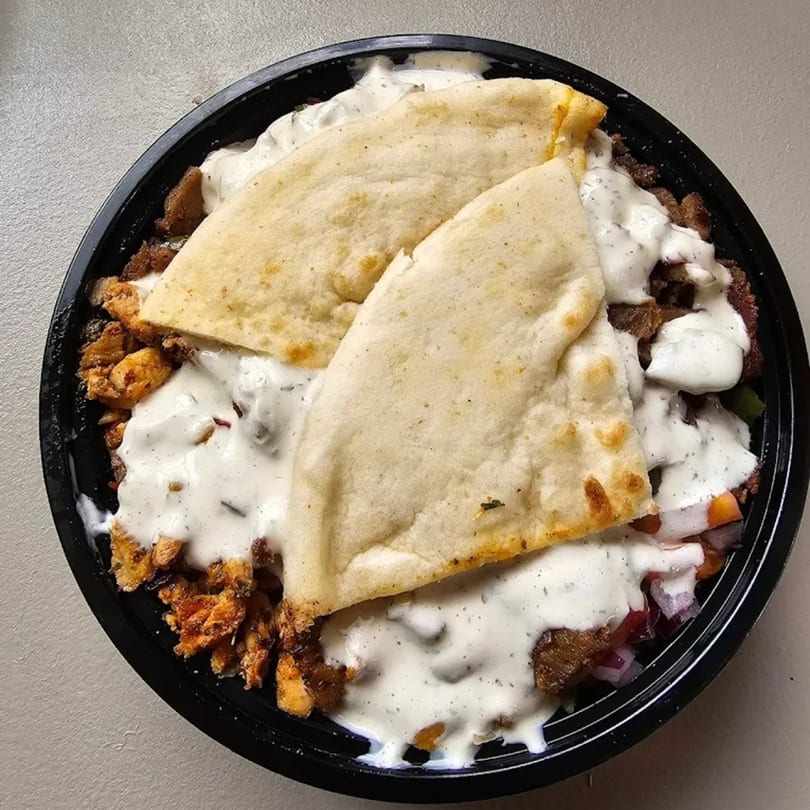 Halal bowl with chicken, beef, white sauce, and two pieces of pita bread in a black bowl.