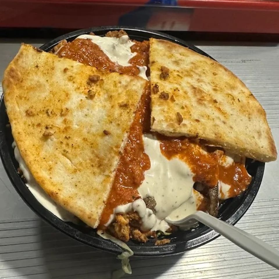 A halal bowl with chicken, red sauce, white sauce, and two pieces of pita bread.