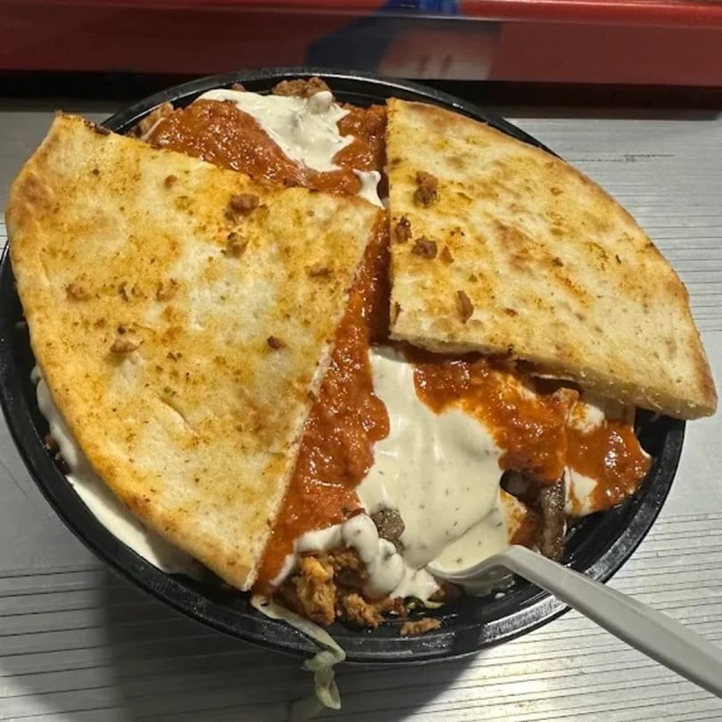 A halal bowl with chicken, red sauce, white sauce, and two pieces of pita bread.